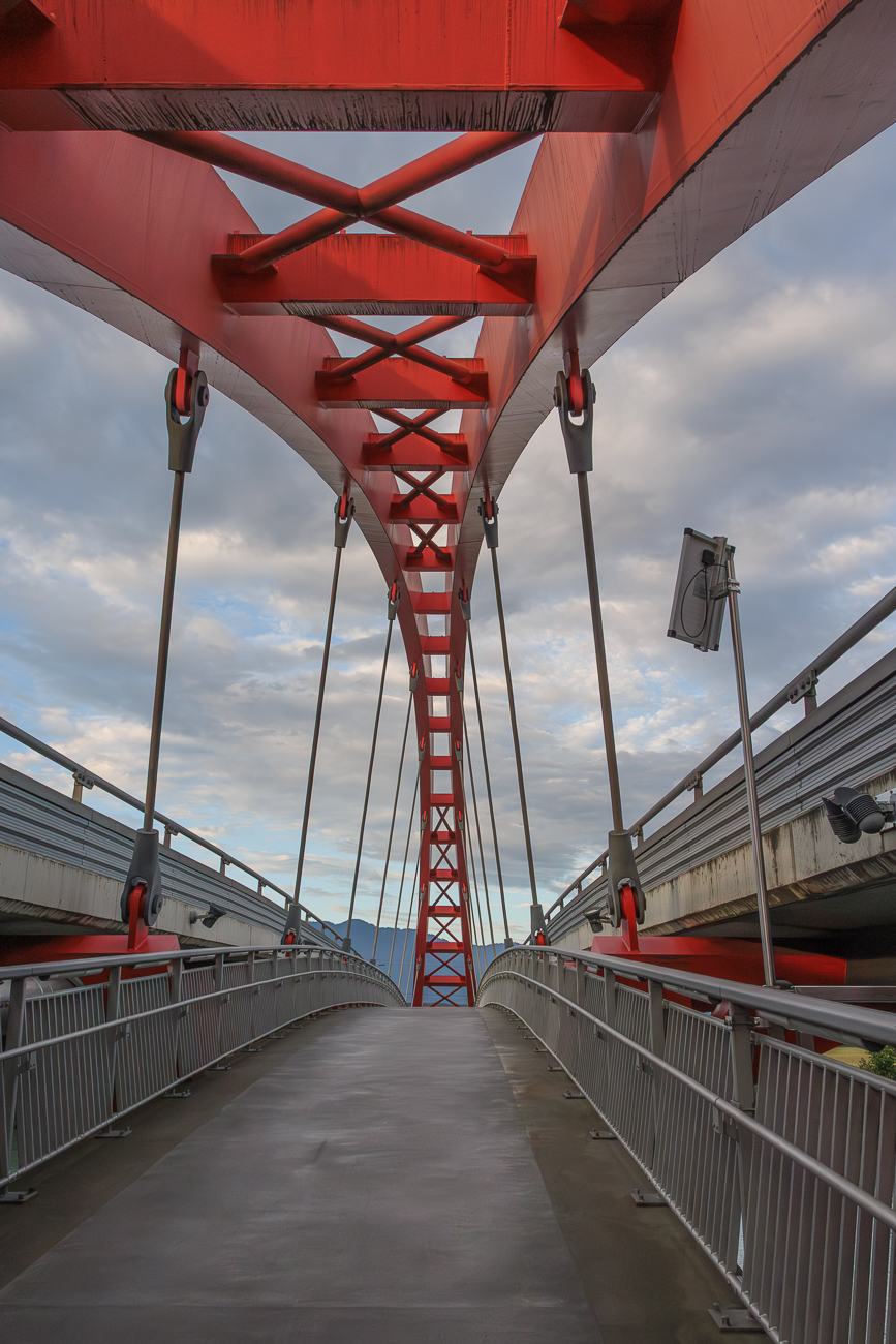 Die Friedensbr&uuml;cke in Villach, eine Bogenbr&uuml;cke, die den Drauweg f&uuml;r Fu&szlig;g&auml;nger und Radfahrer &uuml;berspannt. Die Br&uuml;cke wurde 2004 fertiggestellt und zeichnet sich durch ihre markante rote Stahlkonstruktion aus. Sie ist ein wichtiger Teil des Alpe-Adria-Radwegs und verbindet Stadtgebiete &uuml;ber die Drau